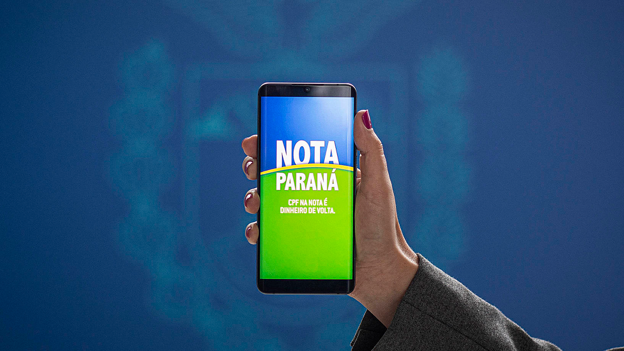 Uma mão de uma mulher ao centro mostra um celular com a frase "Nota Paraná, CPF na nota é dinheiro de volta". 