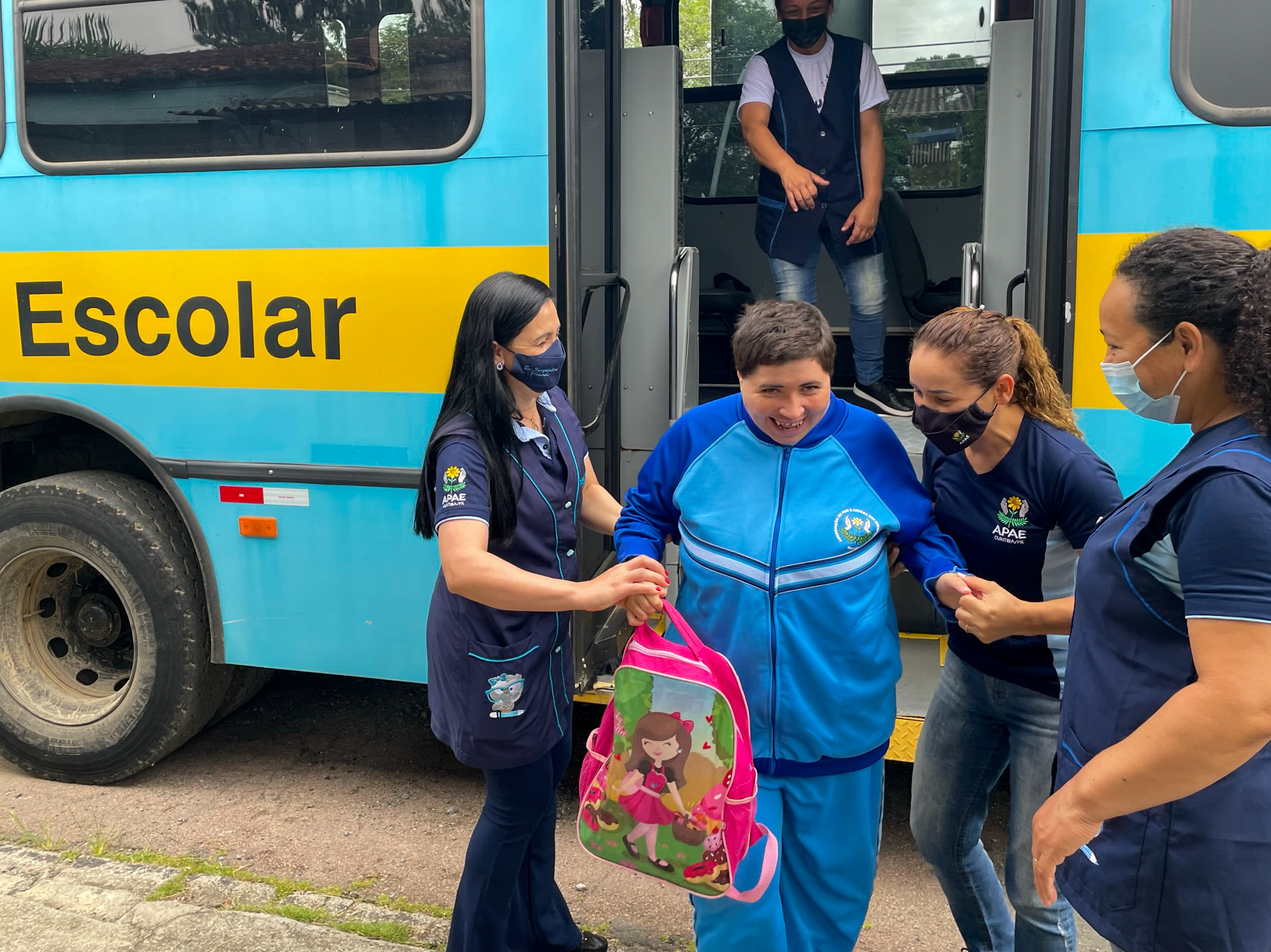 Aluna saindo de dento do ônibus escolar com a ajuda da diretora da Escola Vivenda, Selma, e mais duas funcionárias.