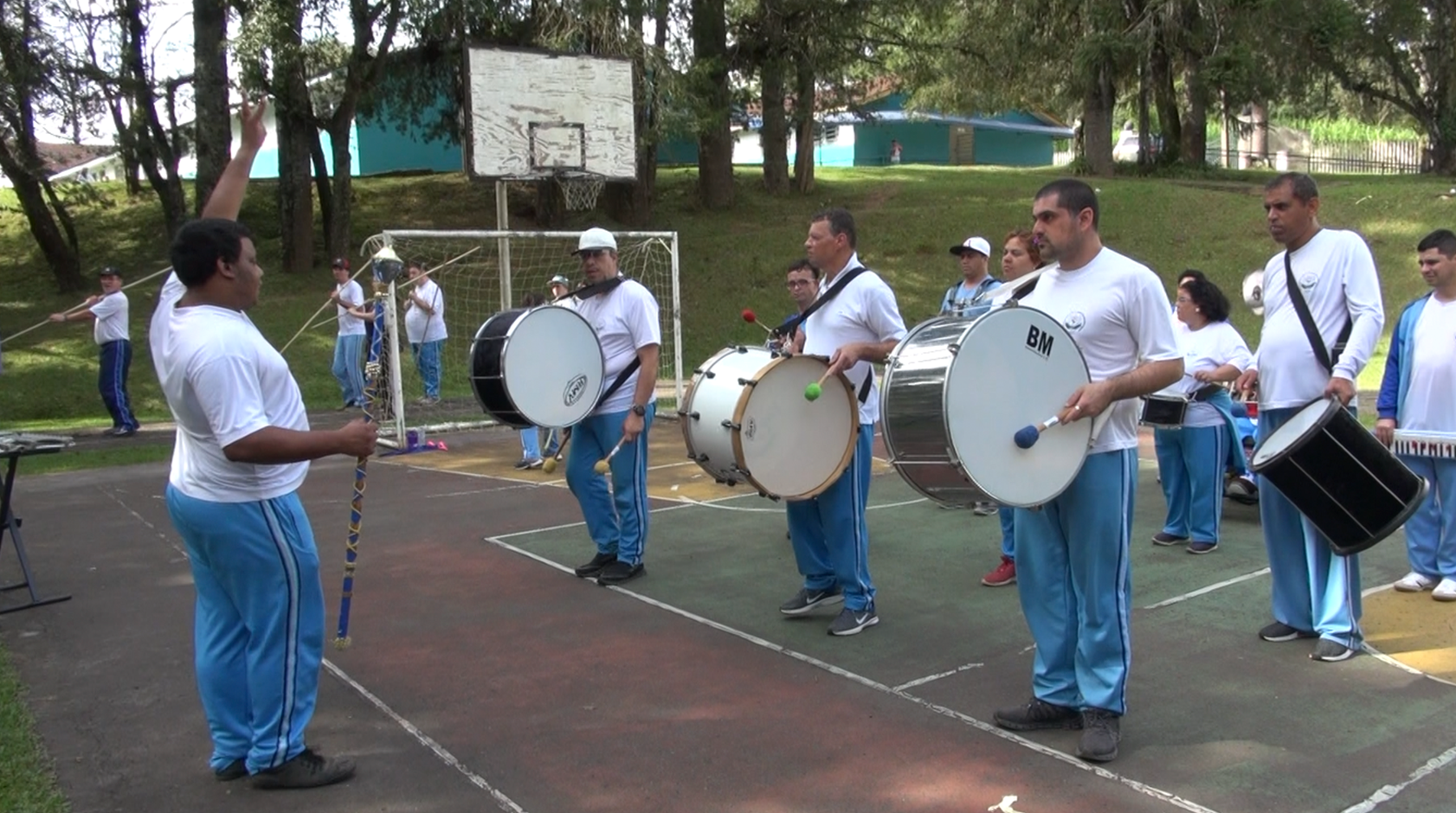Fanfarra da Apae: Alunos estão reunidos na quadra de esportes de uma escola da Apae. Todos enfileirados com instrumentos na mão.