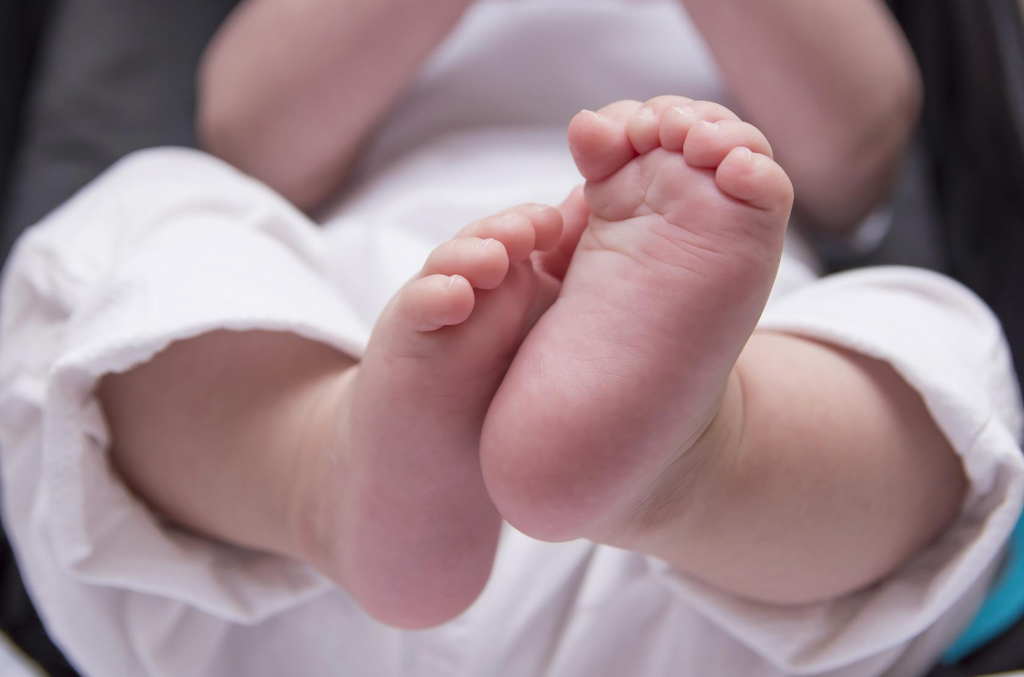 Imagem de um bebê deitado. Apare apenas seu corpo para baixo do pescoço, mas seu pé é o que chama mais atenção no centro da tela