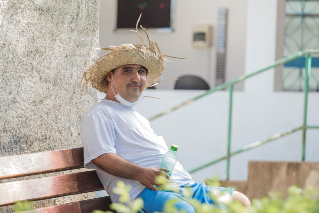 Morador da Casa Lar com um chapéu caipira sentado em um banco que fica aos redores da casa