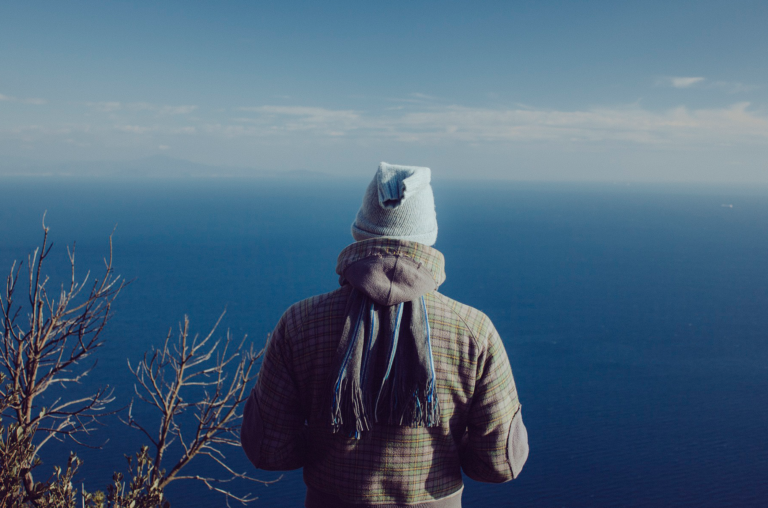 Homem de costas, com roupas de frio, olhando o horizonte