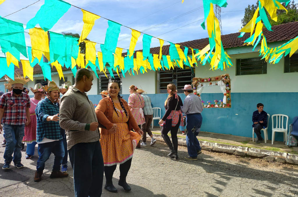alunos prontos para dançar no pátio da escola. Há bandeirinhas de festa junina verdes e amarelas